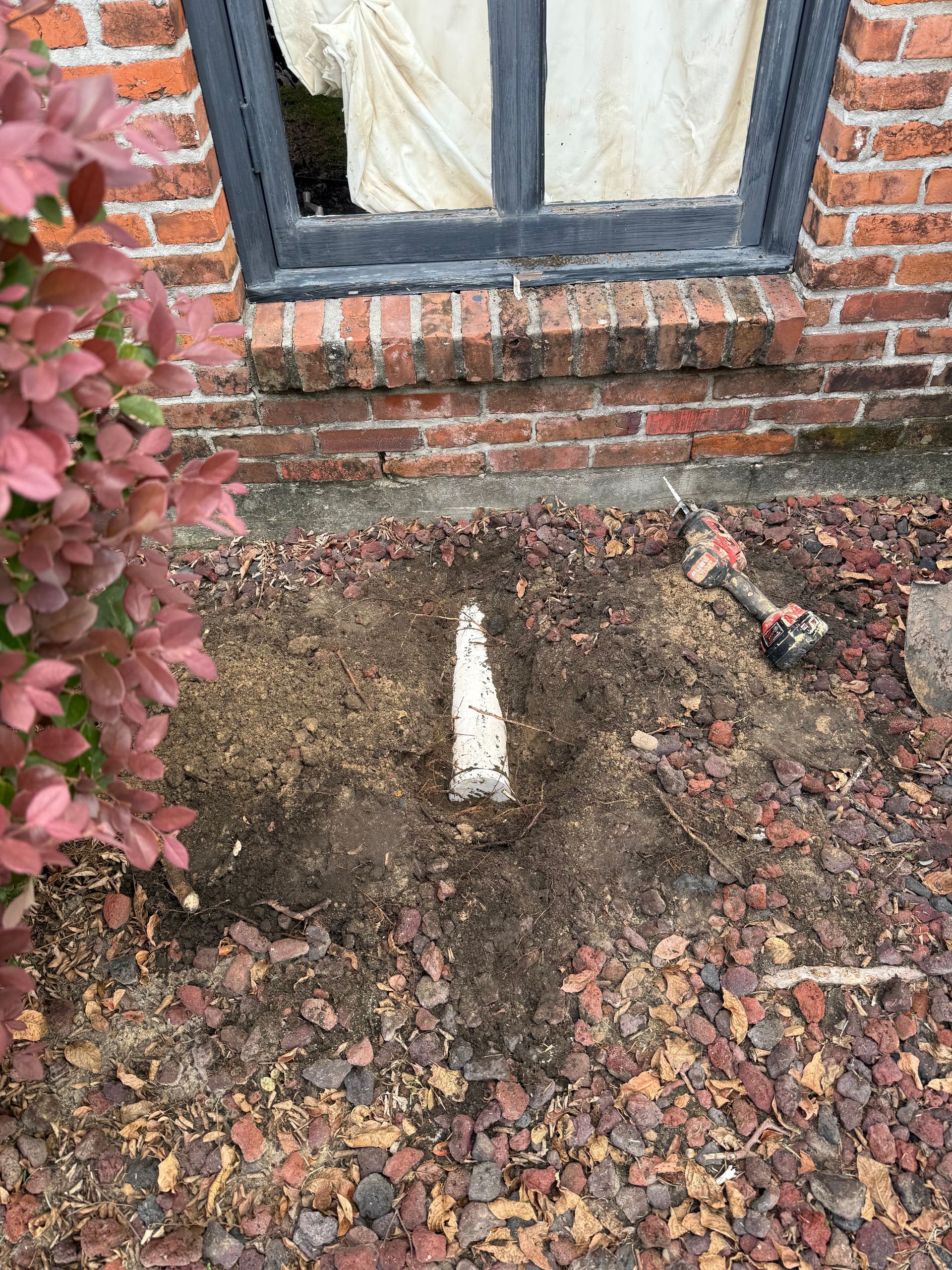 Small white post in a dirt patch by a brick wall and window, with fallen leaves around it
