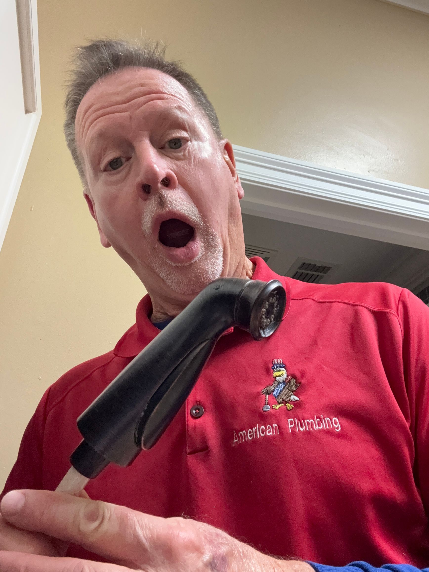 Man in red shirt holding a black curved object, making a surprised expression indoors.