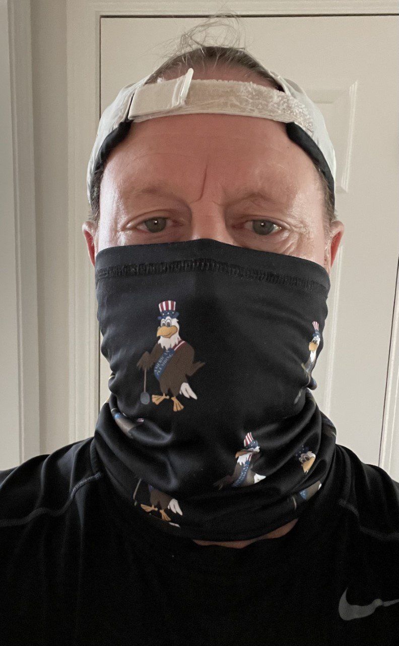 Person wearing a black face covering and gray cap, facing the camera indoors.