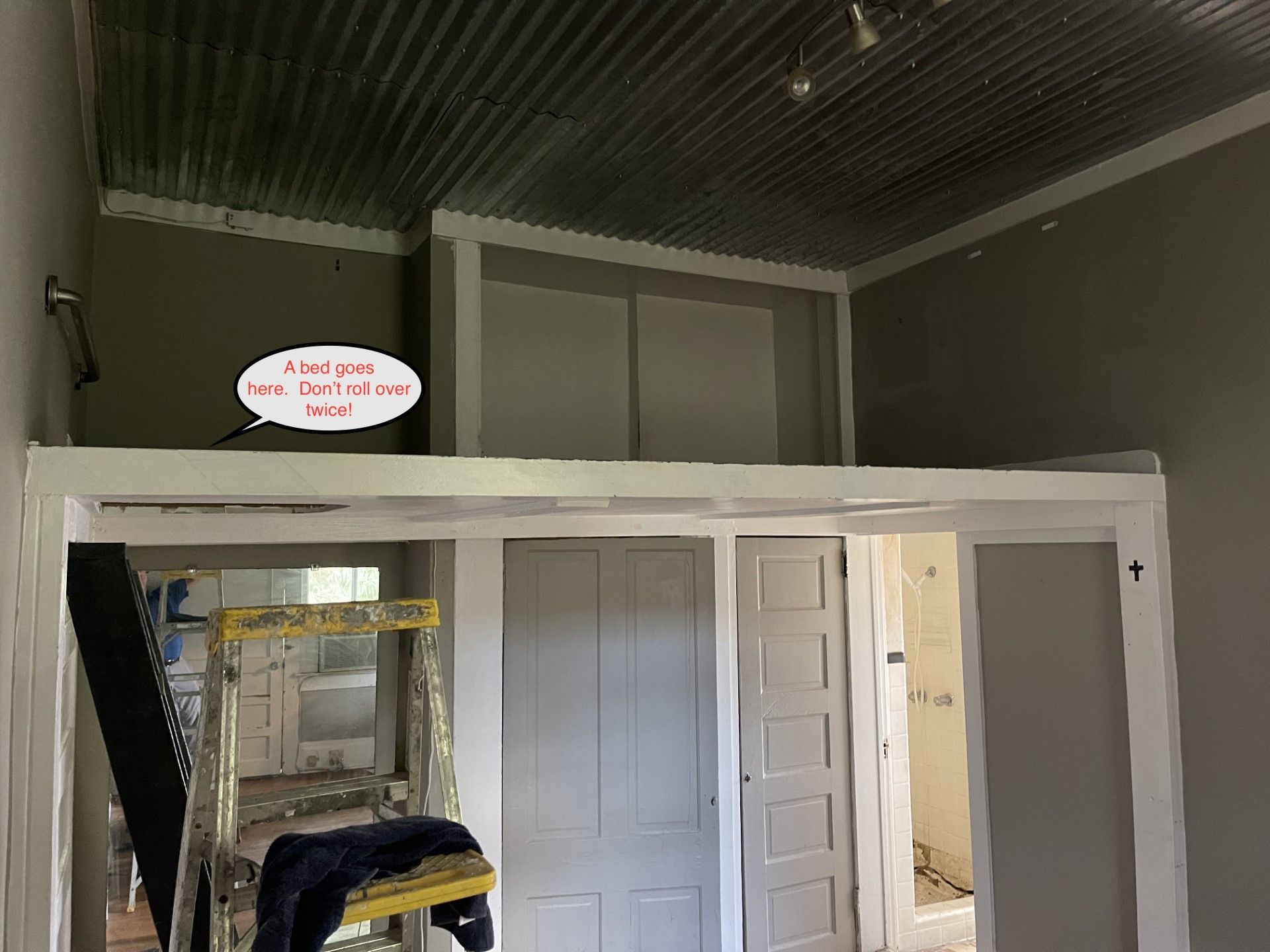 Indoor room with white loft platform, doors, and exposed ceiling beams under renovation