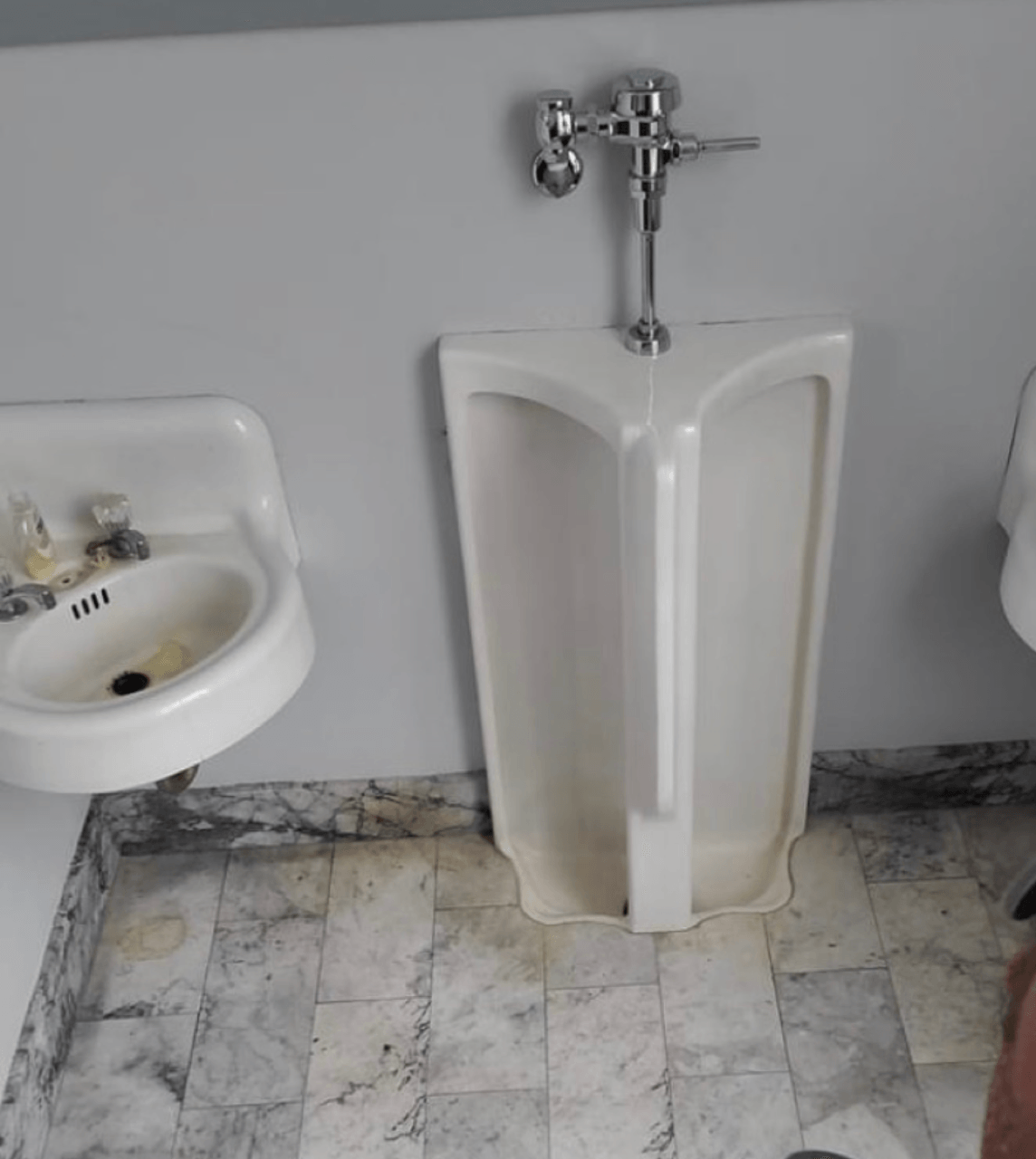 Urinal in public restroom with sink and marble flooring.