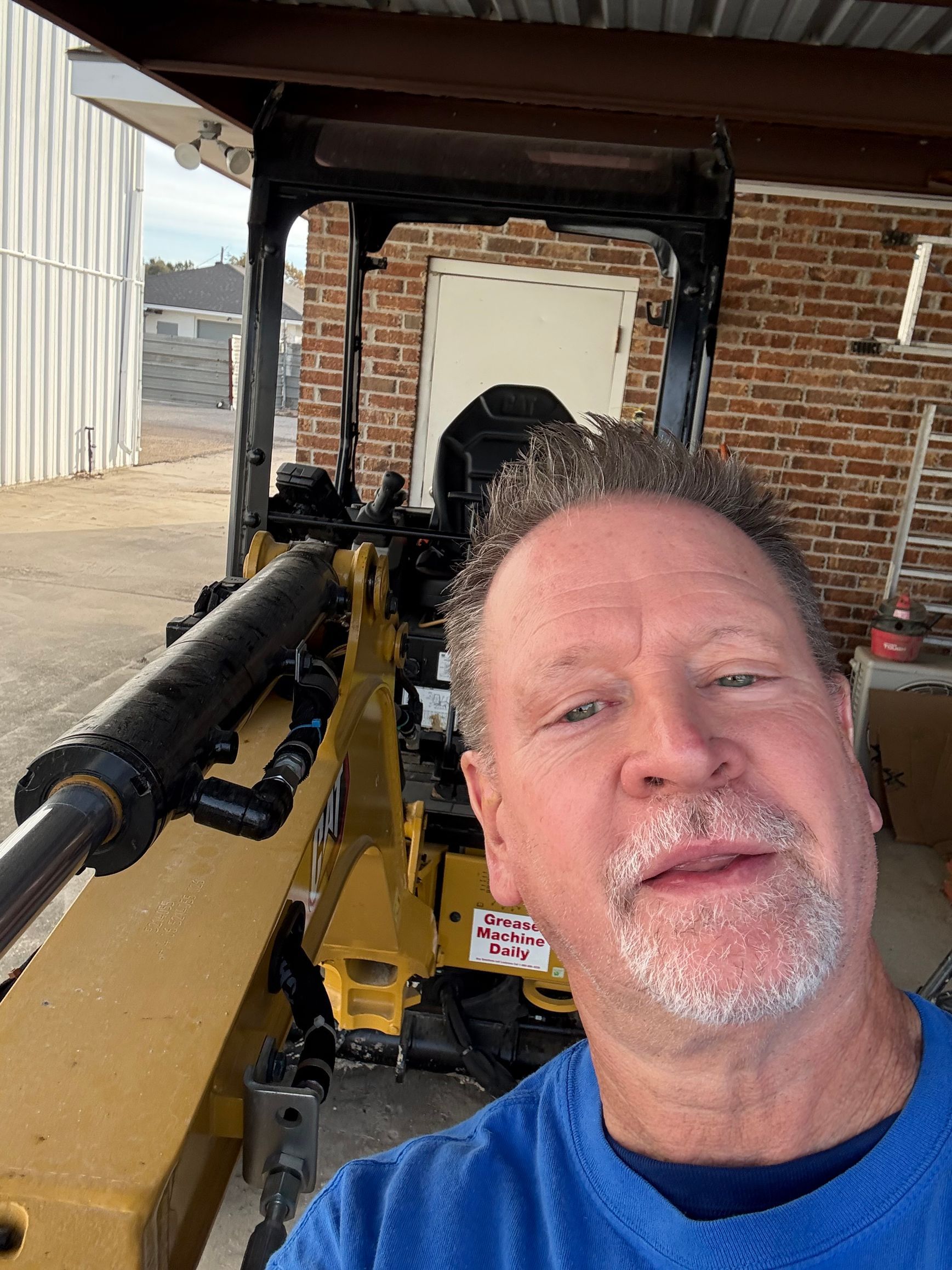 Man posing beside a yellow machine in a brick-and-metal workshop area