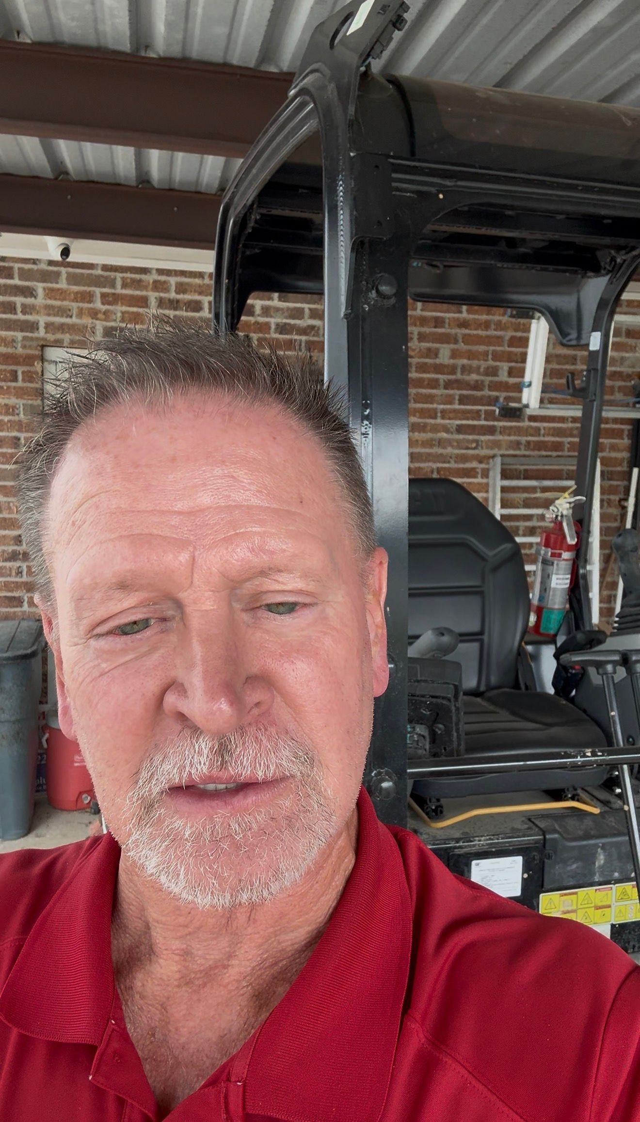 Man in a red shirt taking a selfie in a garage beside a black utility vehicle