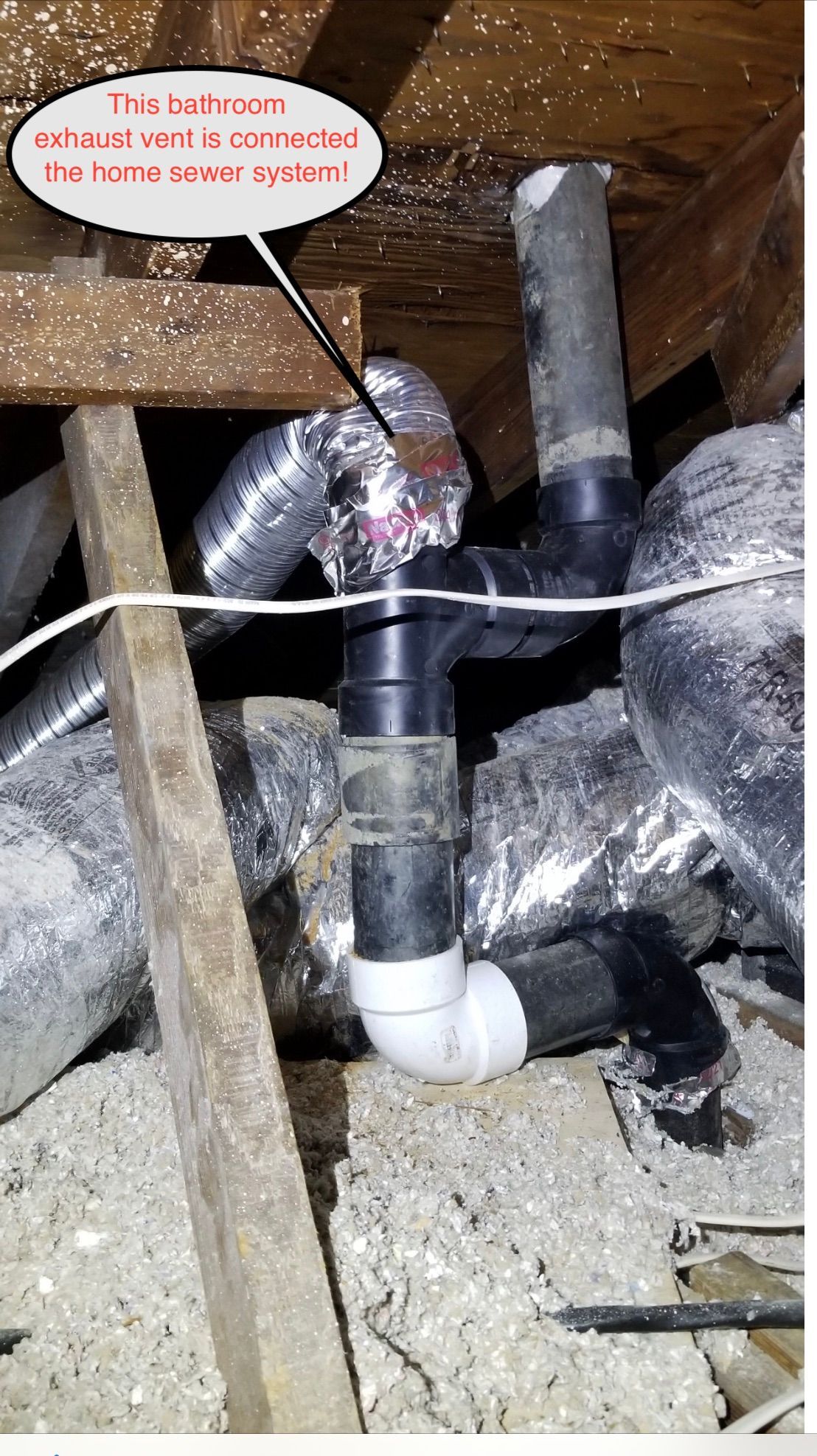Insulated pipes in a crawl space with a red note pointing to a damaged pipe joint