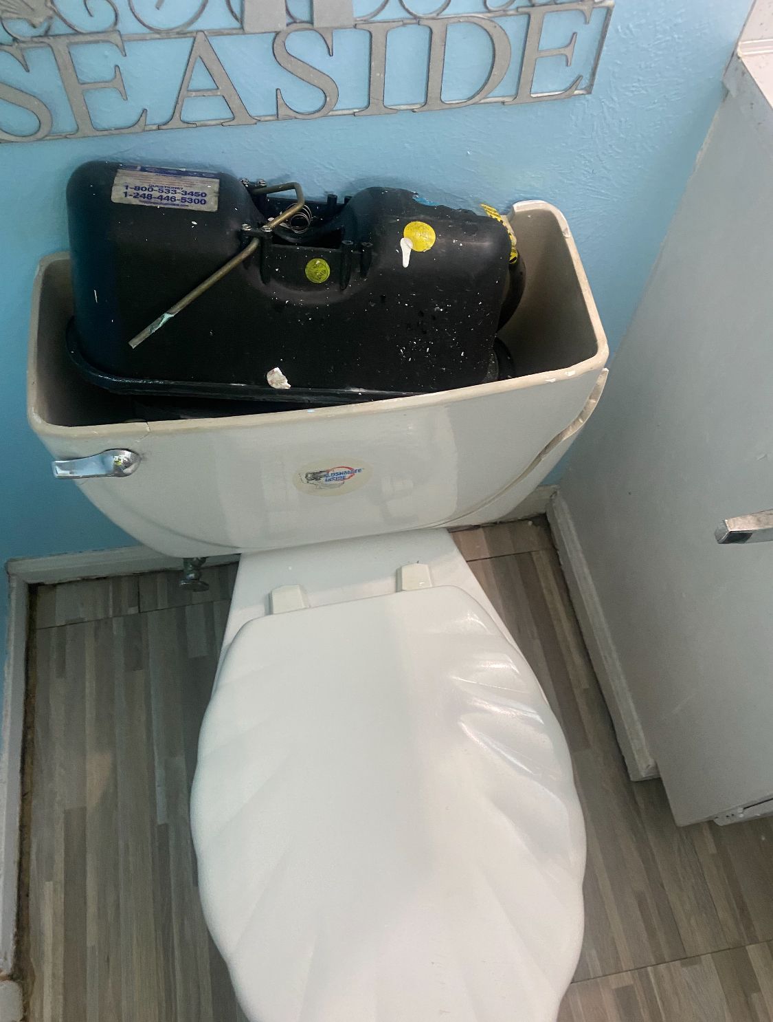 Damaged toilet with black water in the tank, next to a bathroom wall and cabinet.