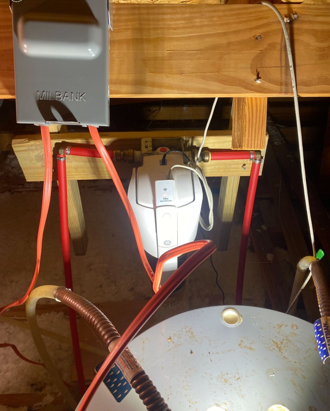 Electrical panel with red wiring, a water heater, and copper pipes in a wooden framework.