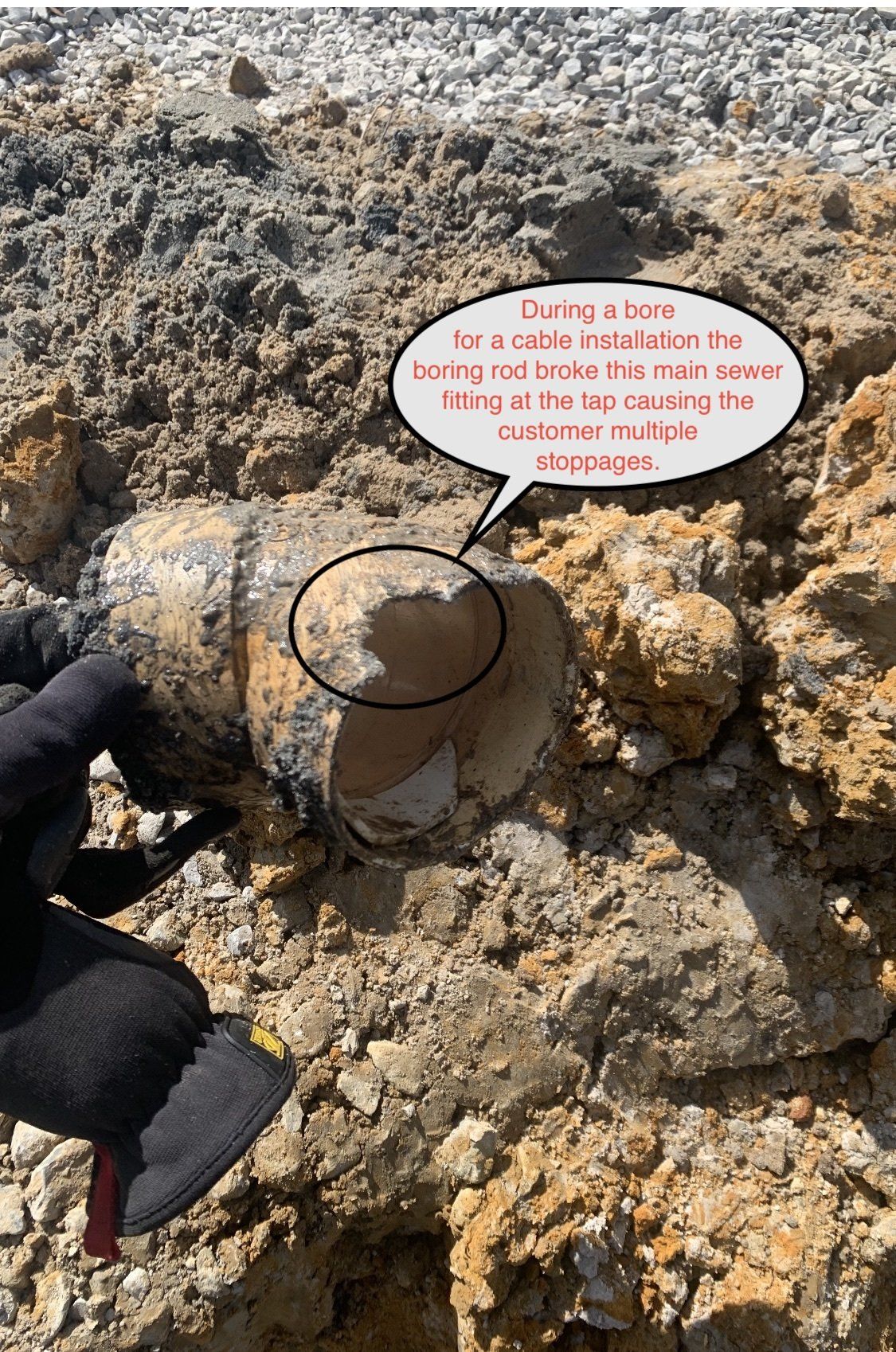 Close-up of a broken, cylindrical object in a hole dug in brown dirt, with a hand wearing a black glove.