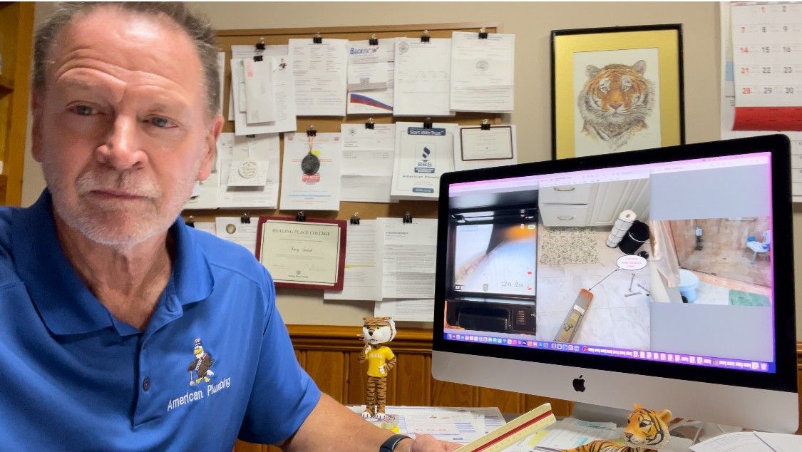 Man in blue shirt on video call; desk with computer, papers, tiger art; concerned expression.