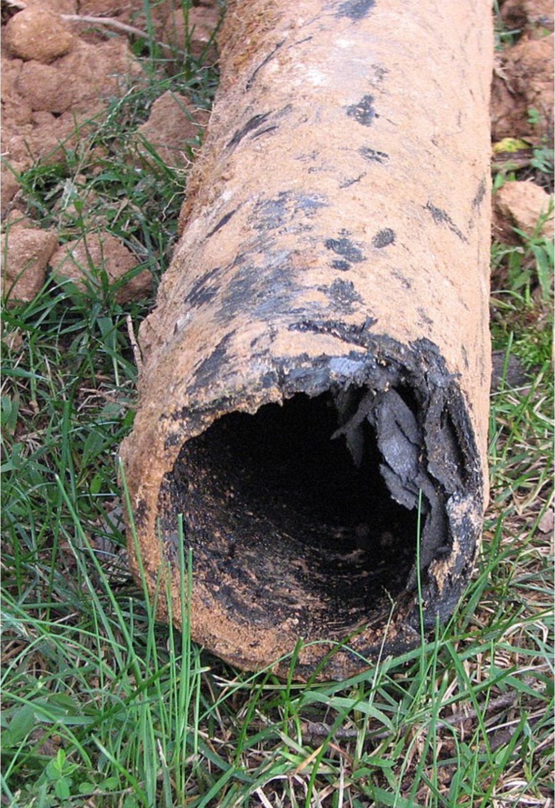 Rusty, broken pipe lying on grass and dirt, with a dark hollow opening exposed