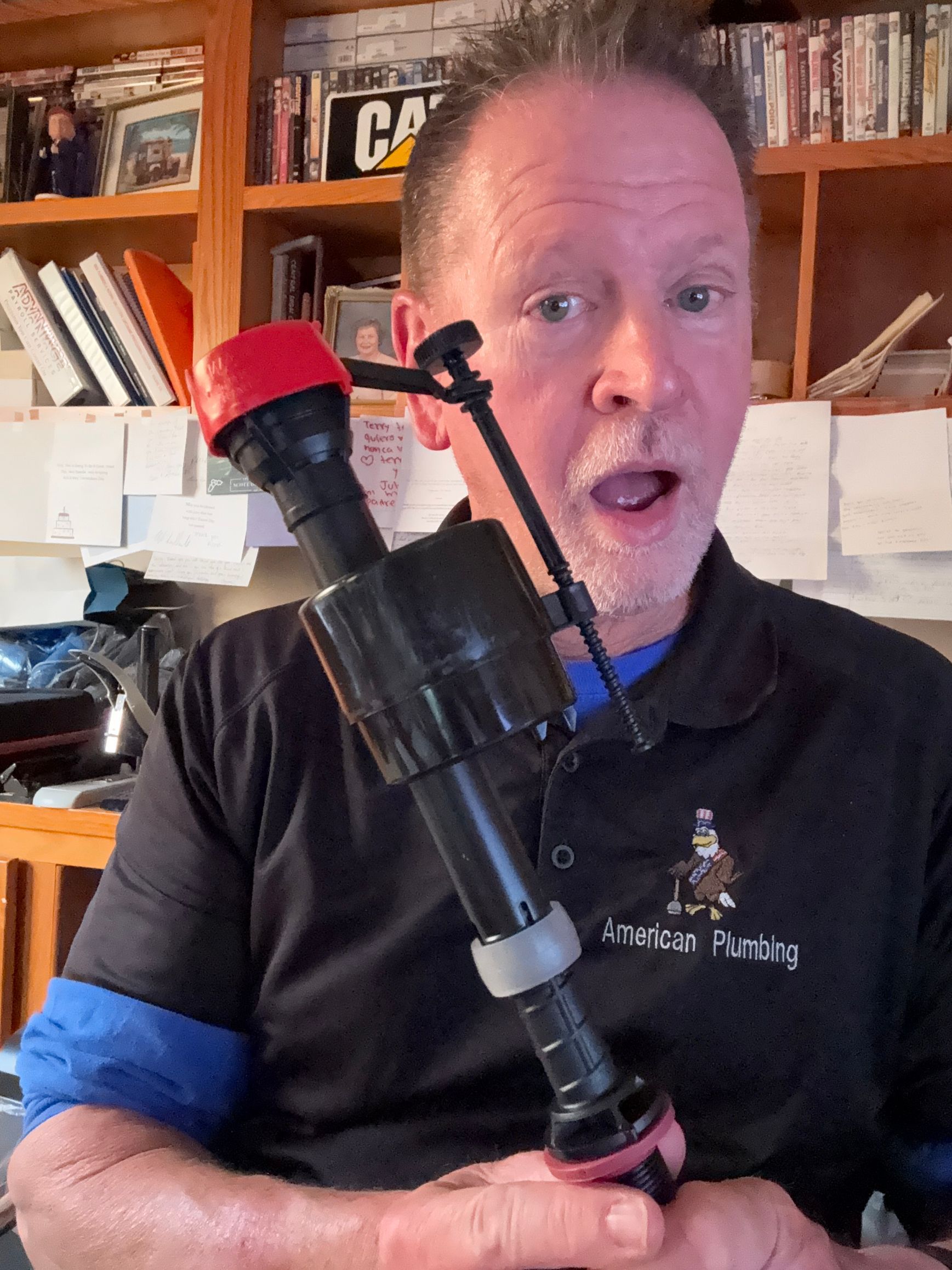 Man holding a black device with a red tip in a home office, shelves and books in the background