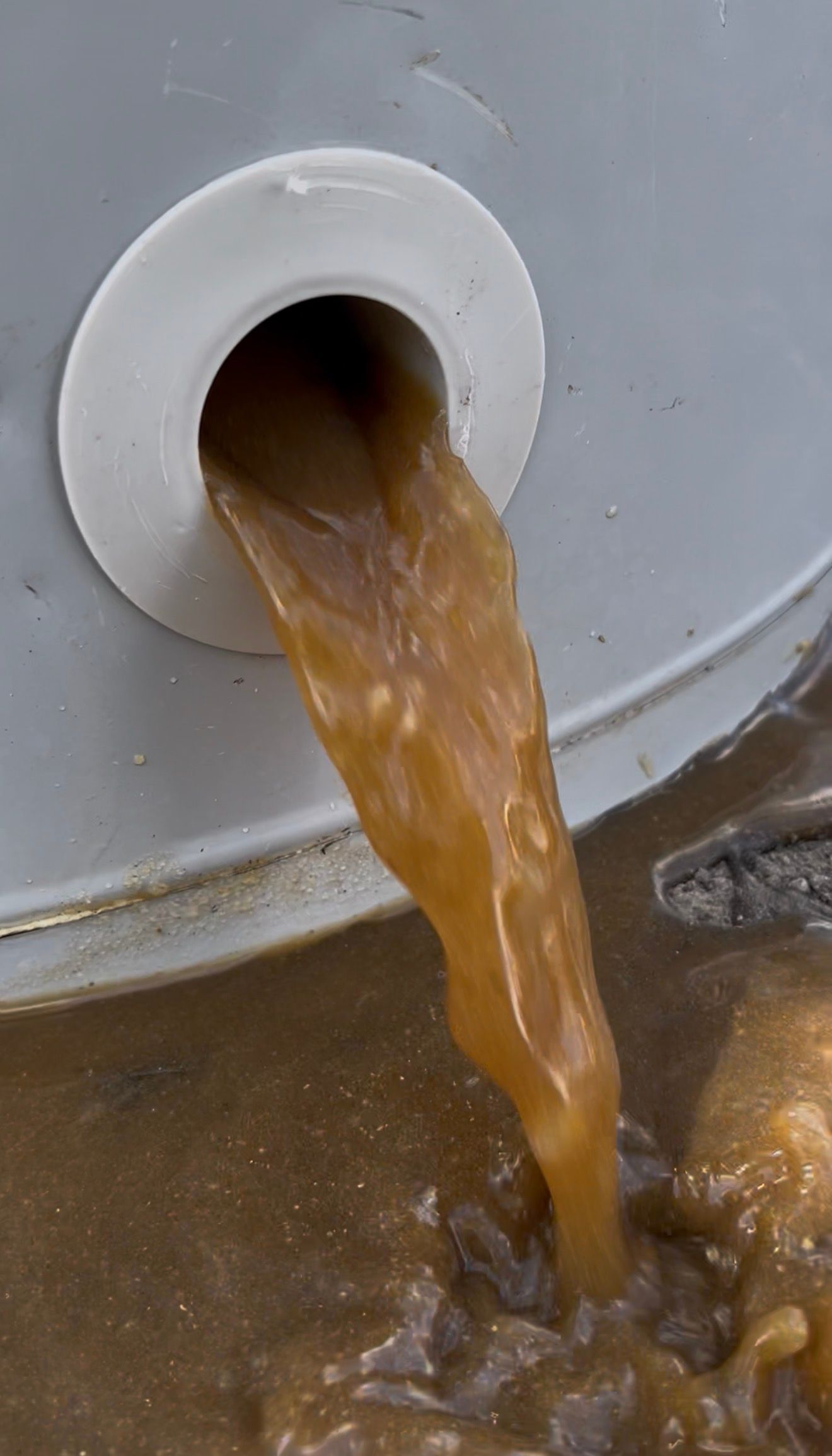 Brown liquid pouring from a white drain pipe into a container