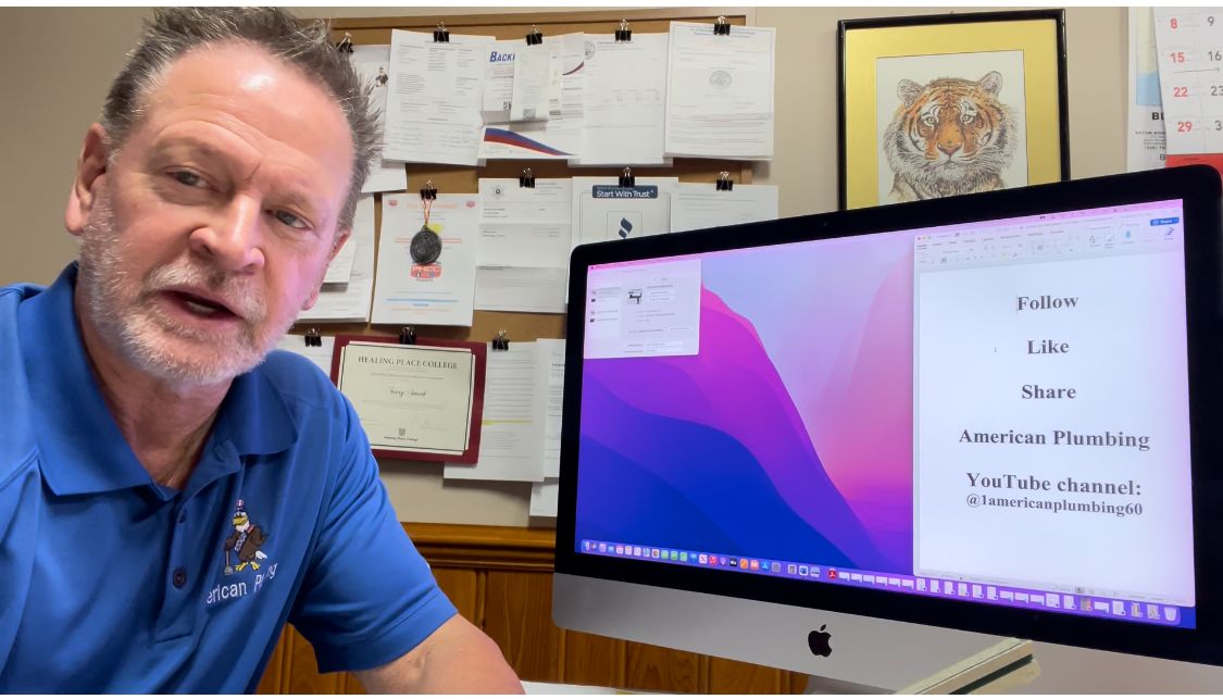 Man in blue shirt speaks while looking at a computer screen displaying text; papers and artwork in background.