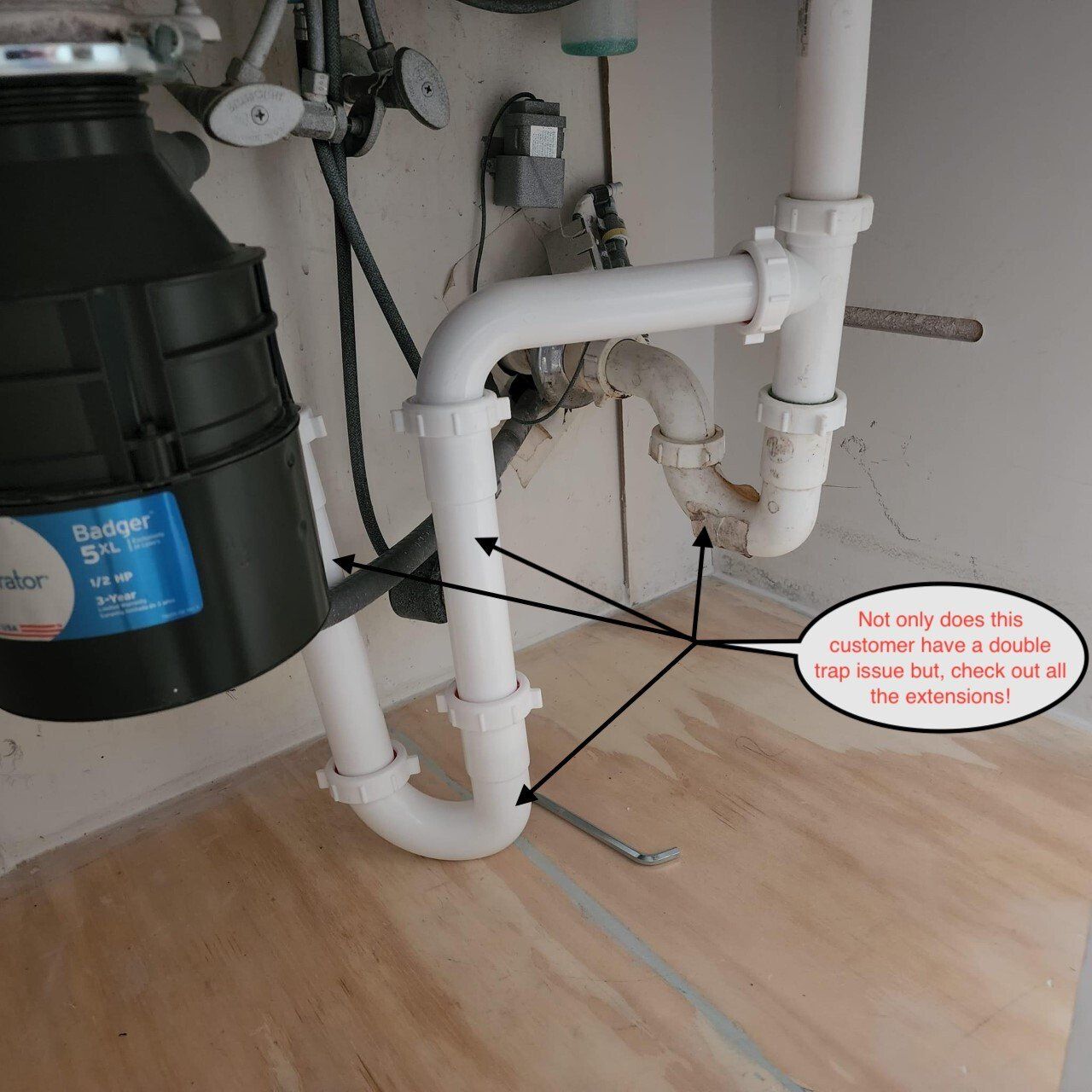 Under-sink plumbing with white pipes and a black water filter canister beneath a cabinet.