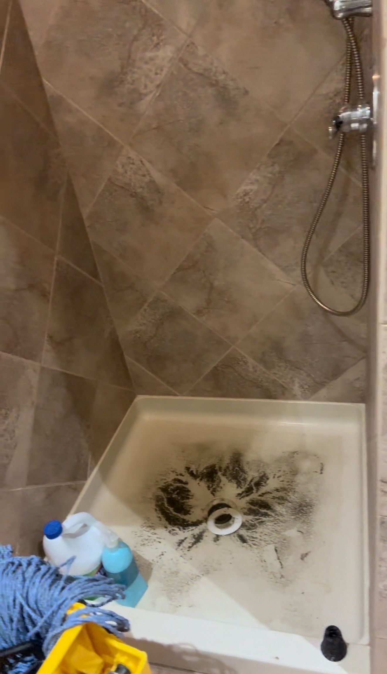Shower corner with beige tile and a dirty white tub stained with dark mold-like residue.