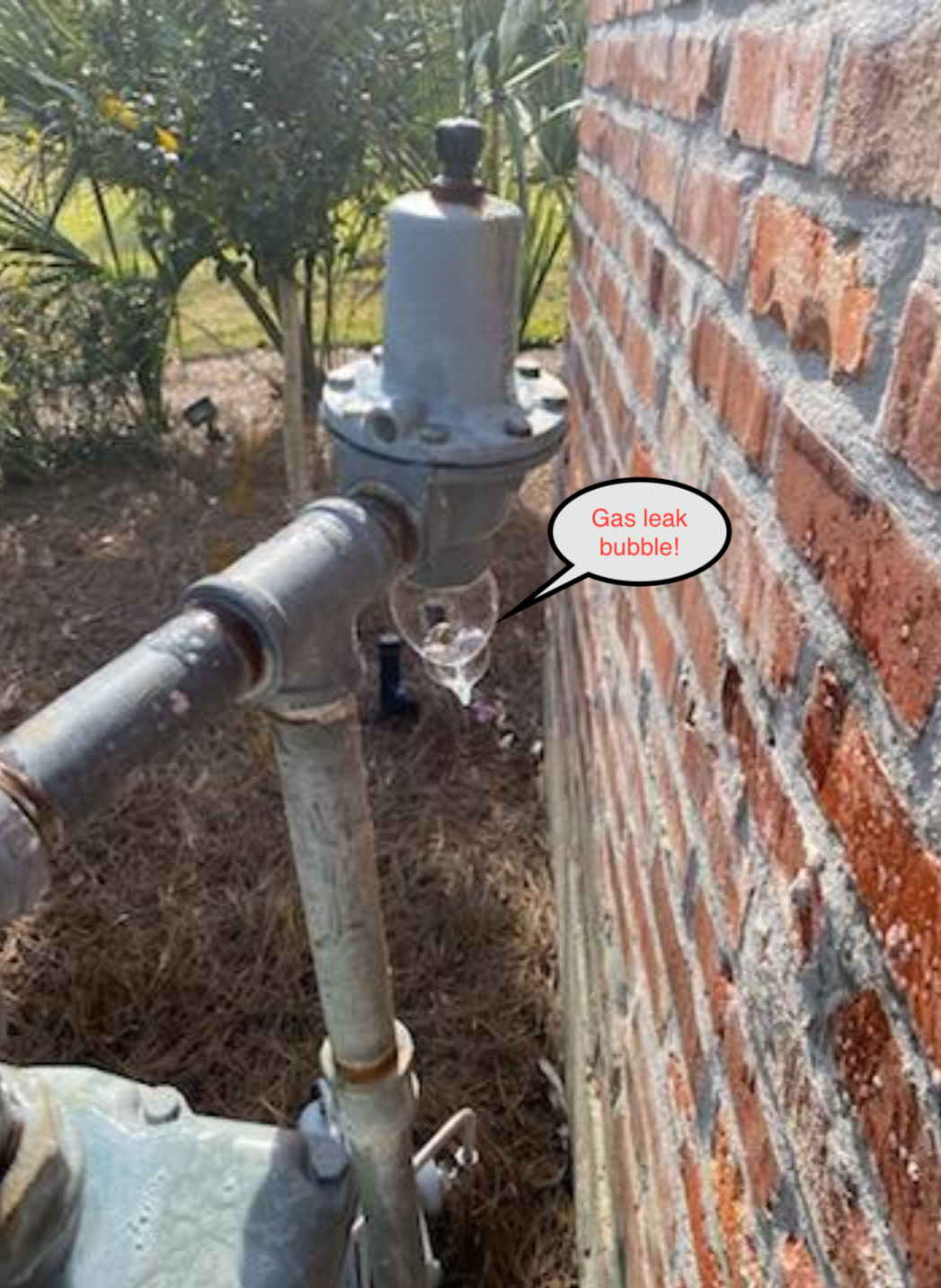 Gas meter and pipe beside a brick wall, with a small label pointing to the shutoff valve.