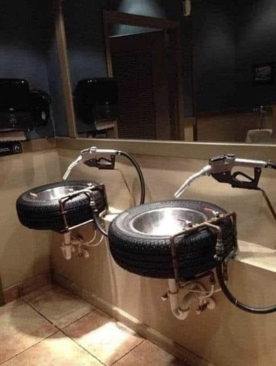 Two sinks made from tires with gas pump handles as faucets in a public restroom.