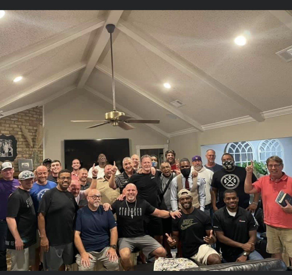 Large group posing together in a living room with vaulted ceiling and ceiling fan, smiling at the camera.