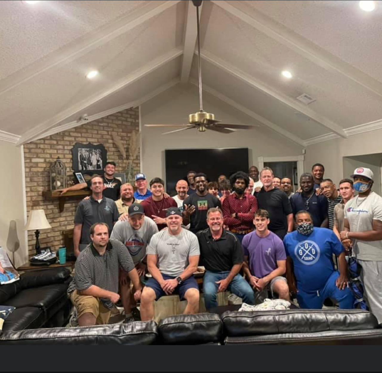 Group of people posing together in a living room with a brick fireplace and ceiling fan.