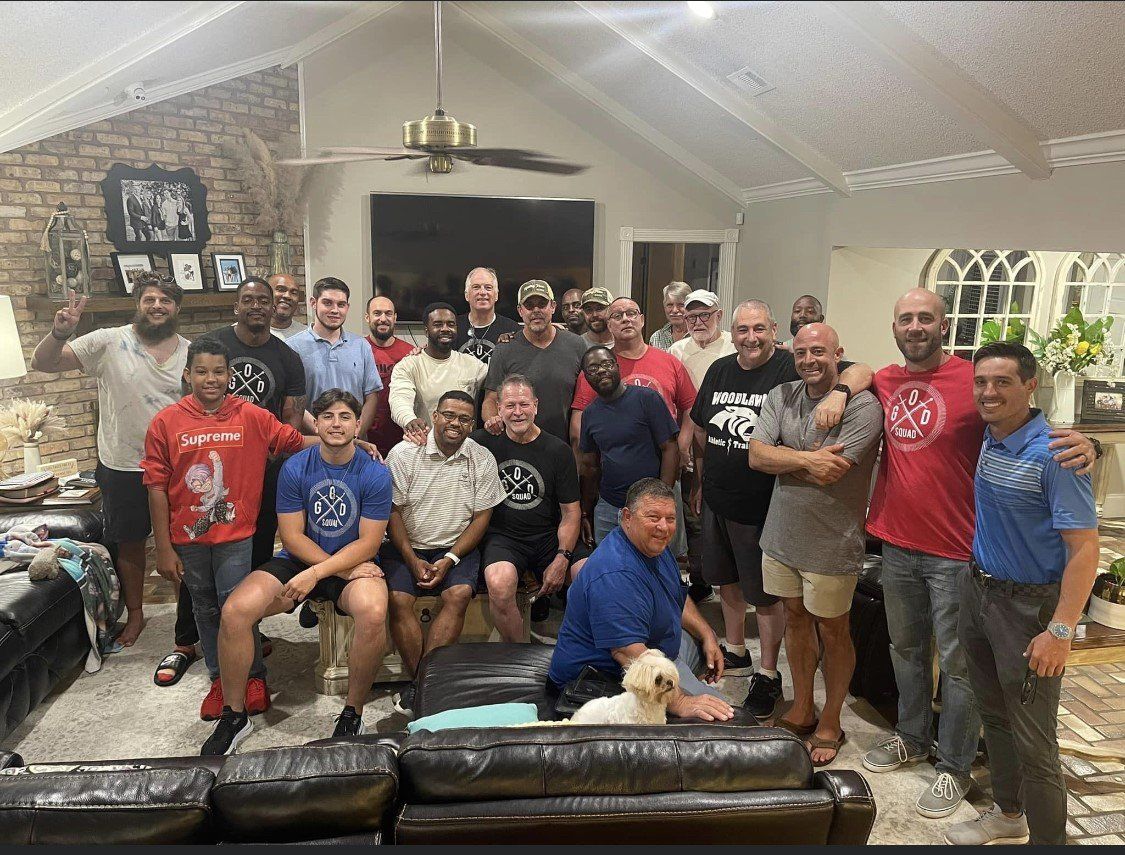 Large group gathered in a living room, posing together with drinks and a small dog on a leather couch.