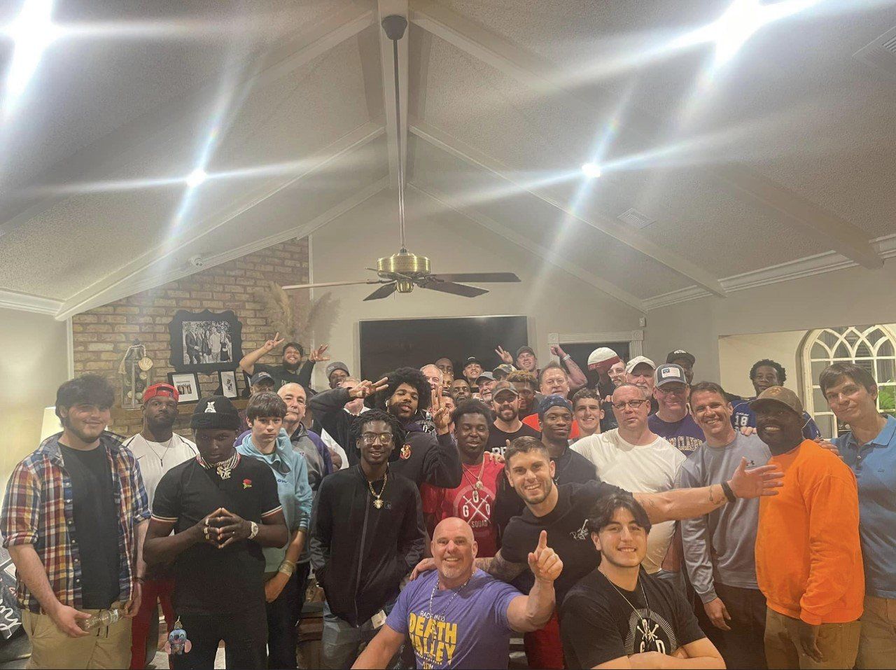 Large group posing together indoors under bright ceiling lights, smiling and gathering for a celebration.