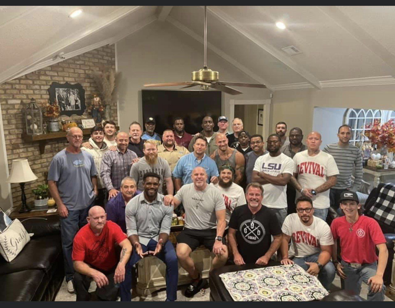 Large group posing together in a living room, smiling around a coffee table with LSU apparel visible.