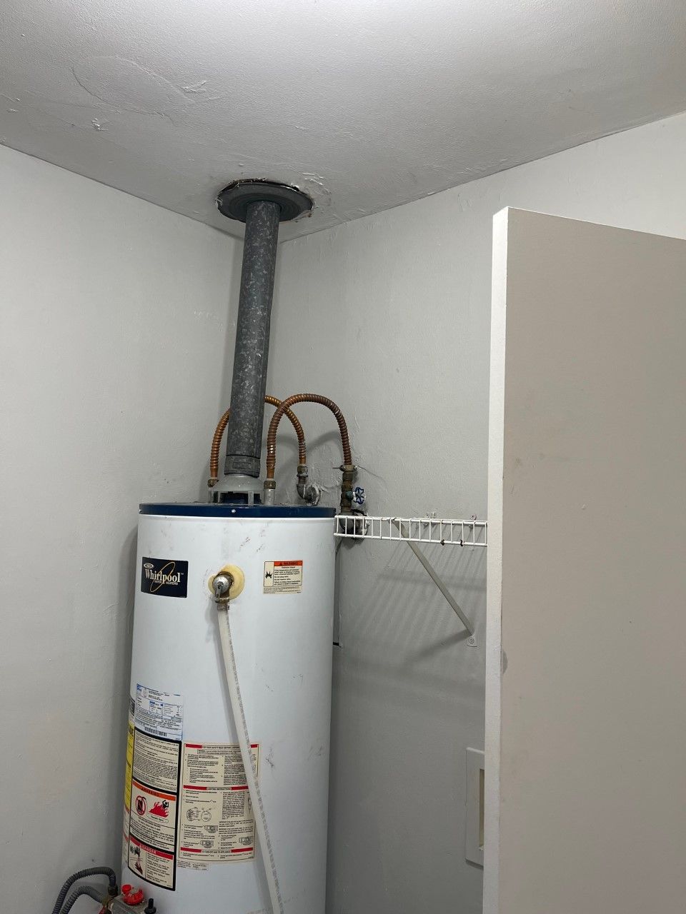 A white water heater with exhaust pipe in a small, white-walled room.