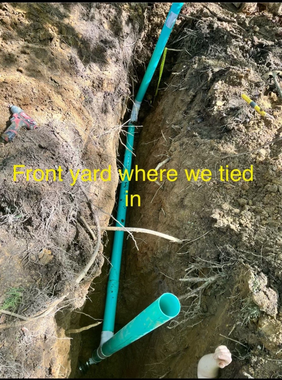 Trench in front yard with a green pipe and tied-in hose between soil and rock walls