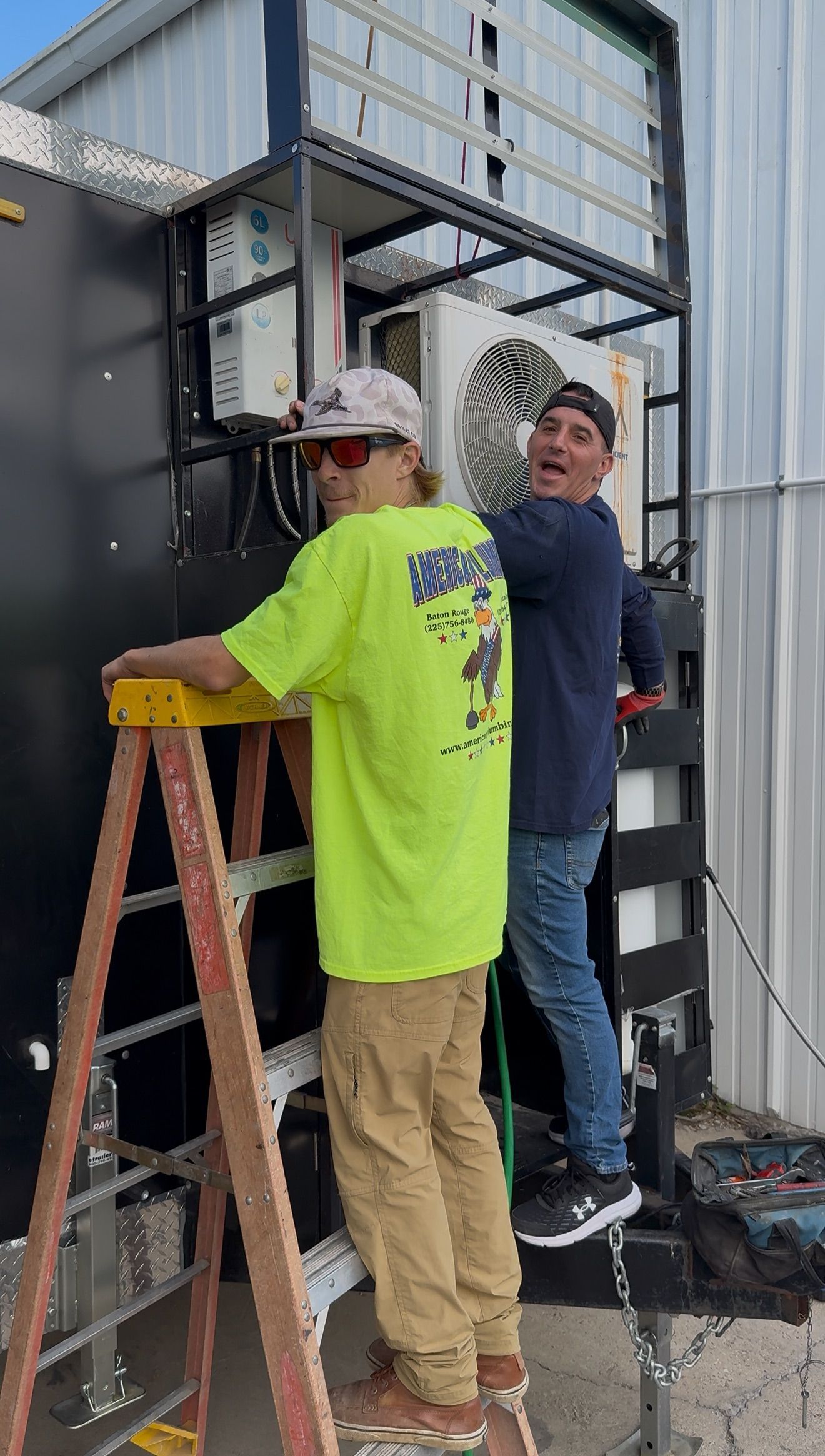 Two workers installing equipment on a metal structure, one on a ladder and one standing below.