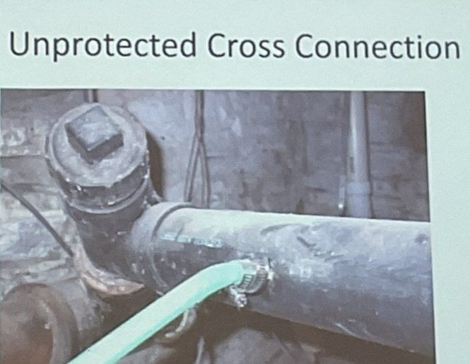 Unprotected pipe cross connection with a green hose attached in an industrial setting