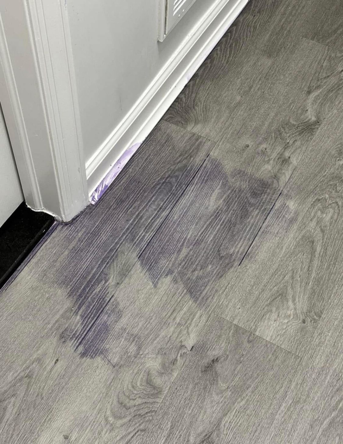 Gray wood-look flooring with a large, dark stain near a white door frame.