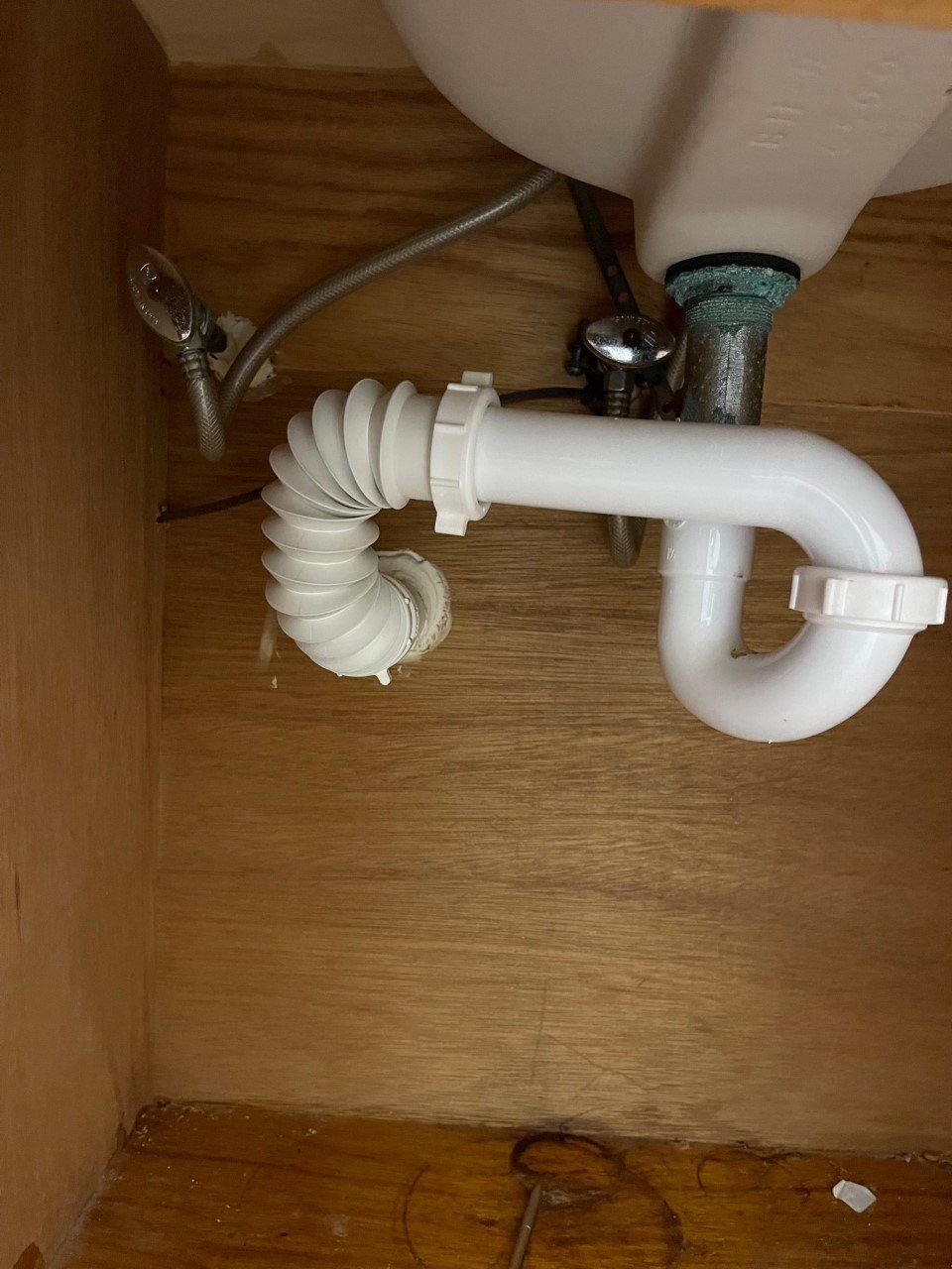 White flexible sink drain pipe under a bathroom sink inside a wooden cabinet.