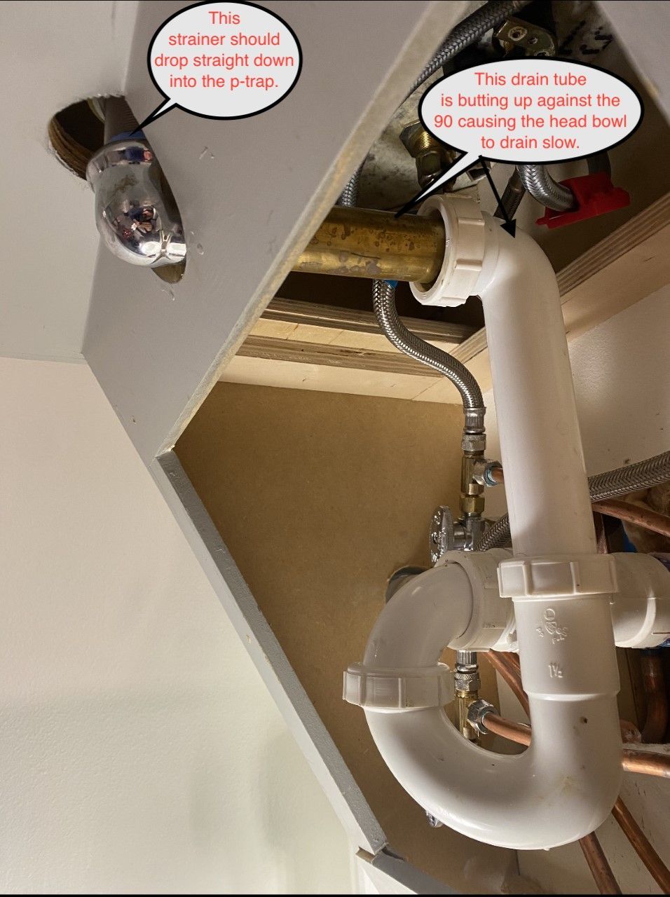 Underside view of sink plumbing. The drain tube is angled, and the water valve is on the right.