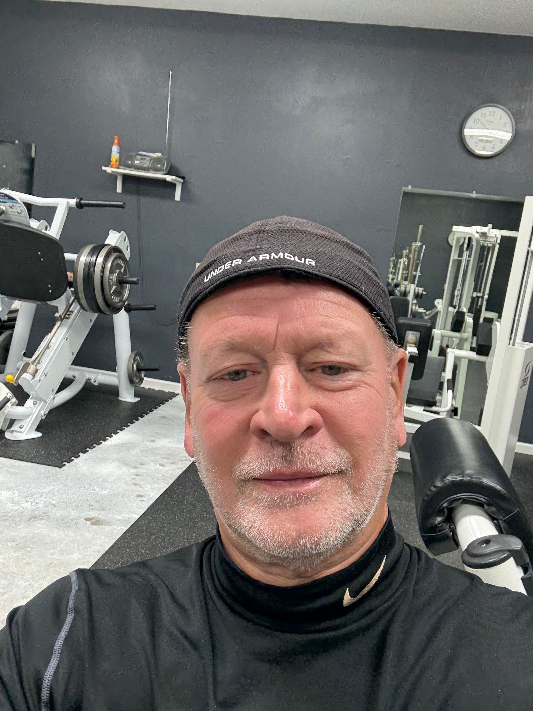 Man taking a selfie in a gym with exercise equipment and dark walls behind him