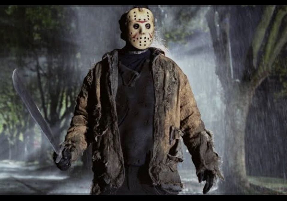 Masked figure in a tattered jacket standing in a rainy forest at night