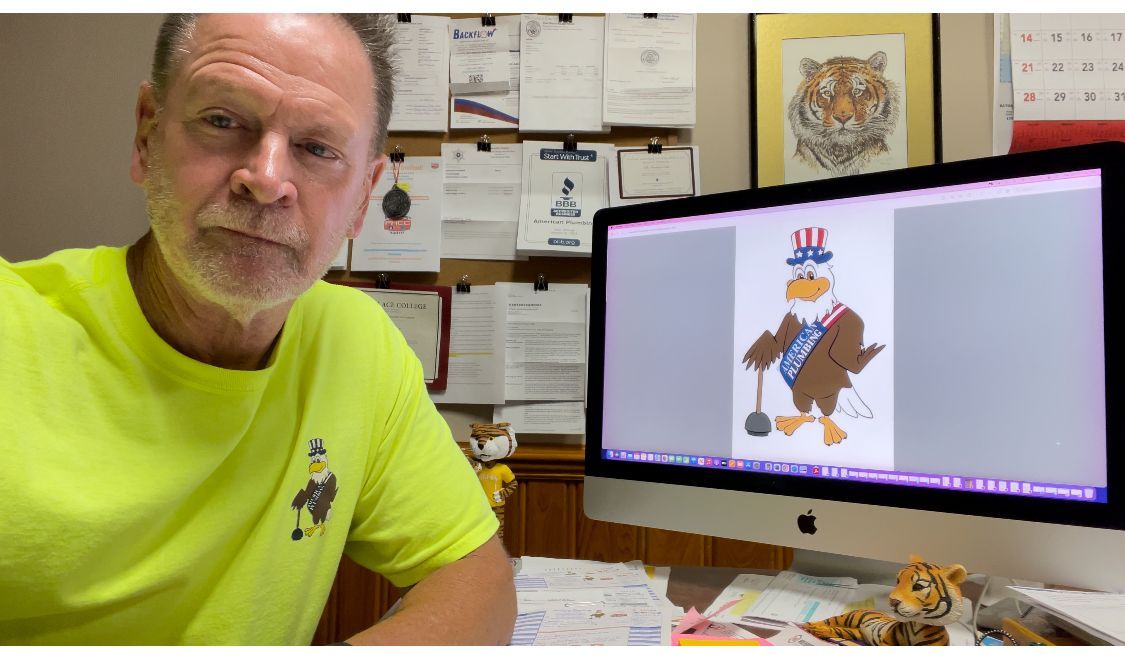Man in neon yellow shirt beside a computer monitor showing a cartoon drawing in an office
