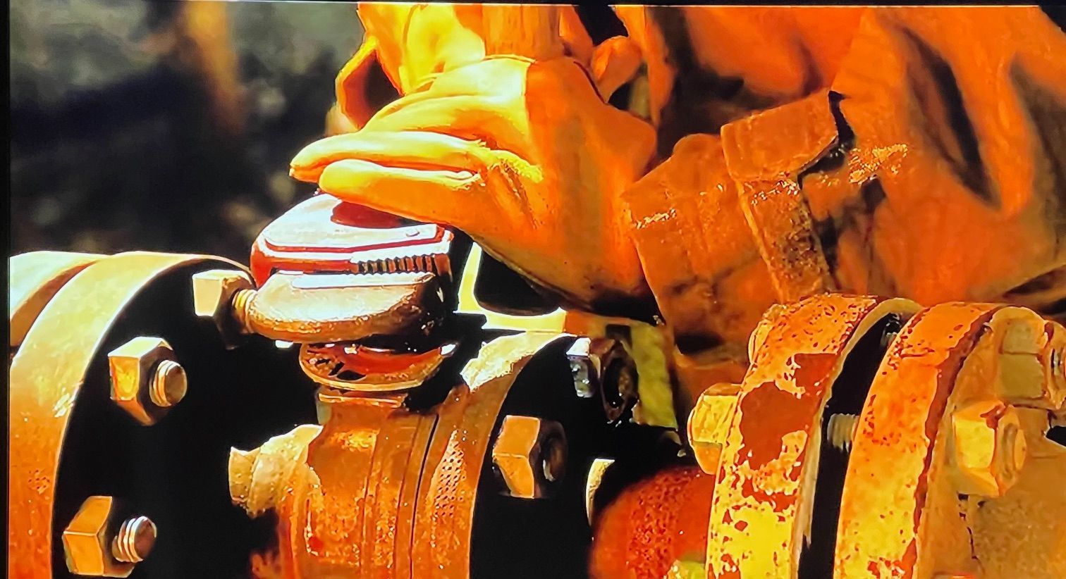 Orange-gloved hand adjusting a valve on yellow industrial piping and fittings