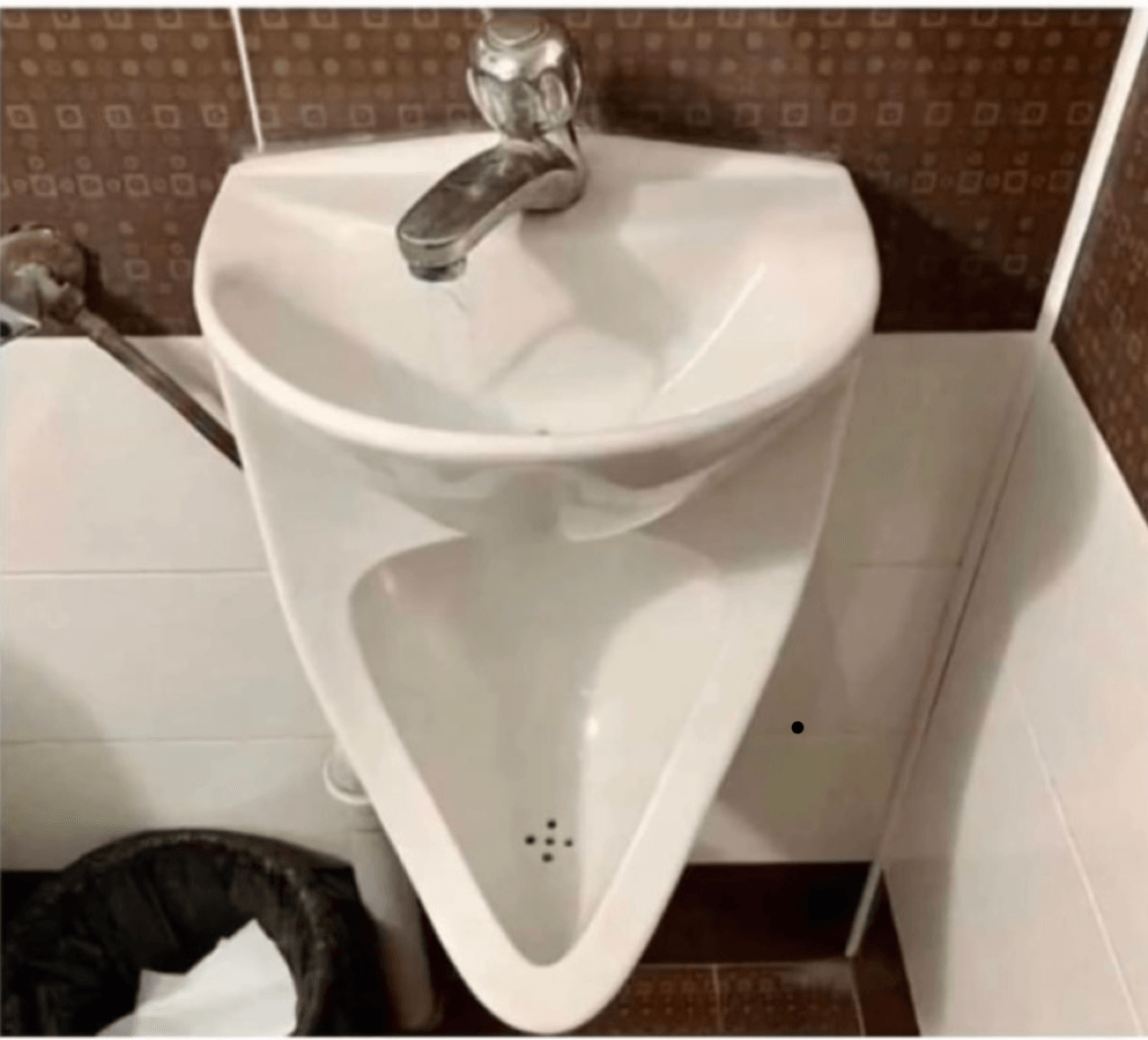 White triangular sink with faucet in a bathroom, mounted on white and brown tiled wall.