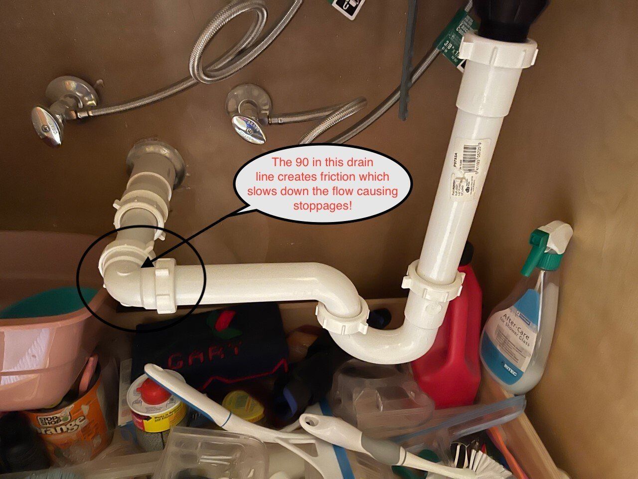 Under-sink plumbing with white PVC pipes, valves, and cleaning supplies in a cabinet