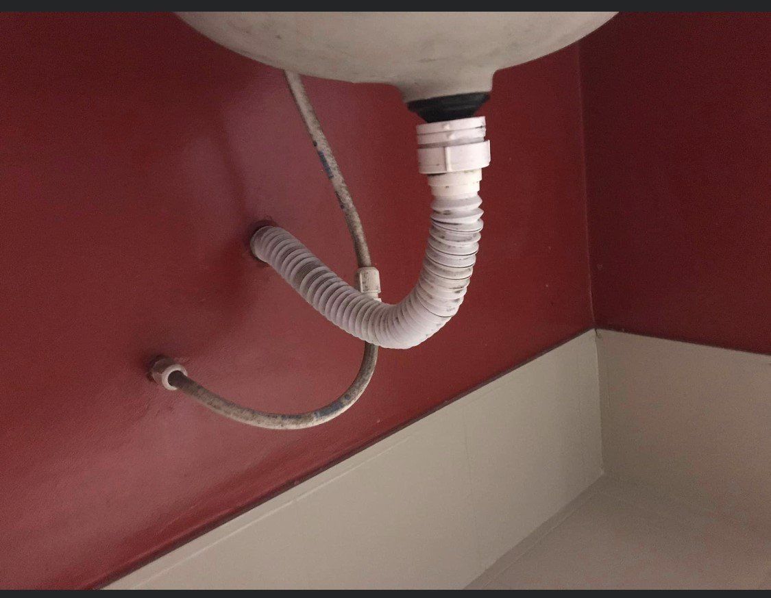 Under-sink plumbing with a white drain pipe against a red wall and beige baseboard