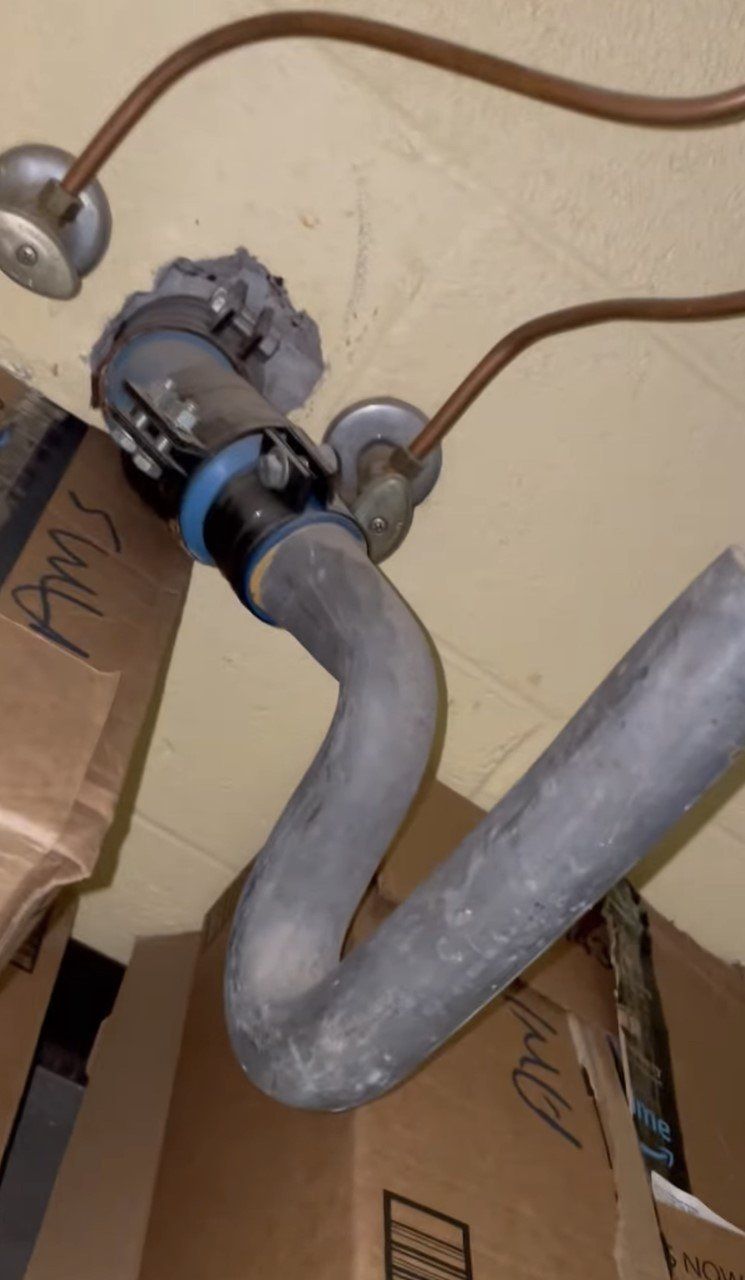 Gray plumbing pipes under a sink, with attached drain and copper water lines.