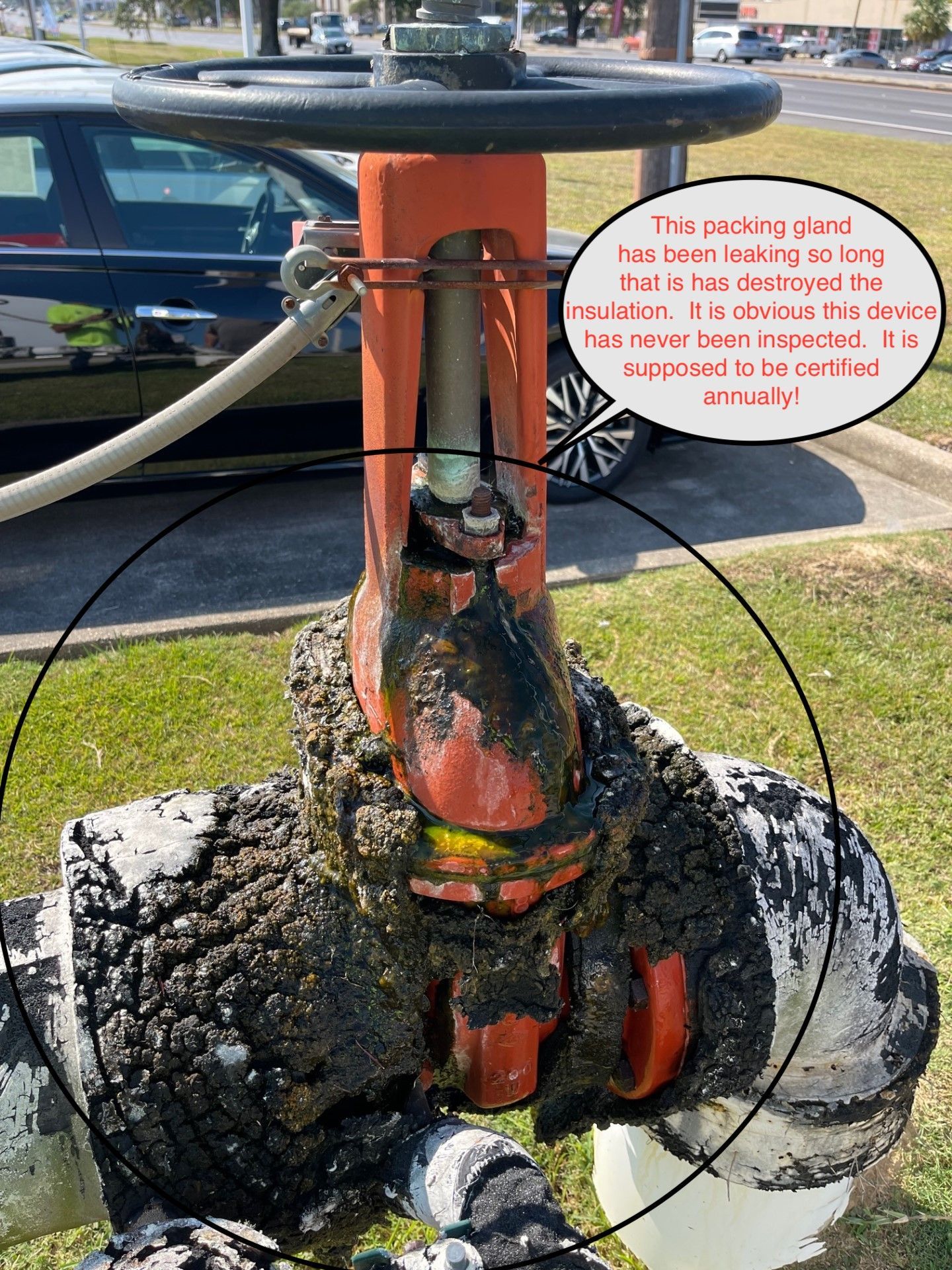 A corroded orange valve covered in oily residue; located outdoors, text indicates long-term leak, possibly uncertified.