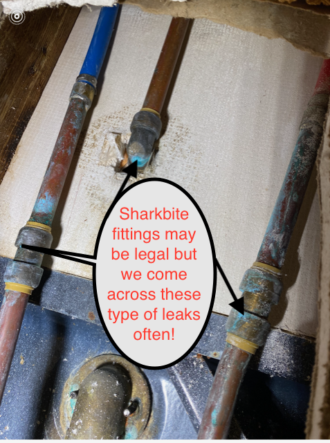 Close-up of three water pipes with leaky sharkbite fittings, one with a red warning note.