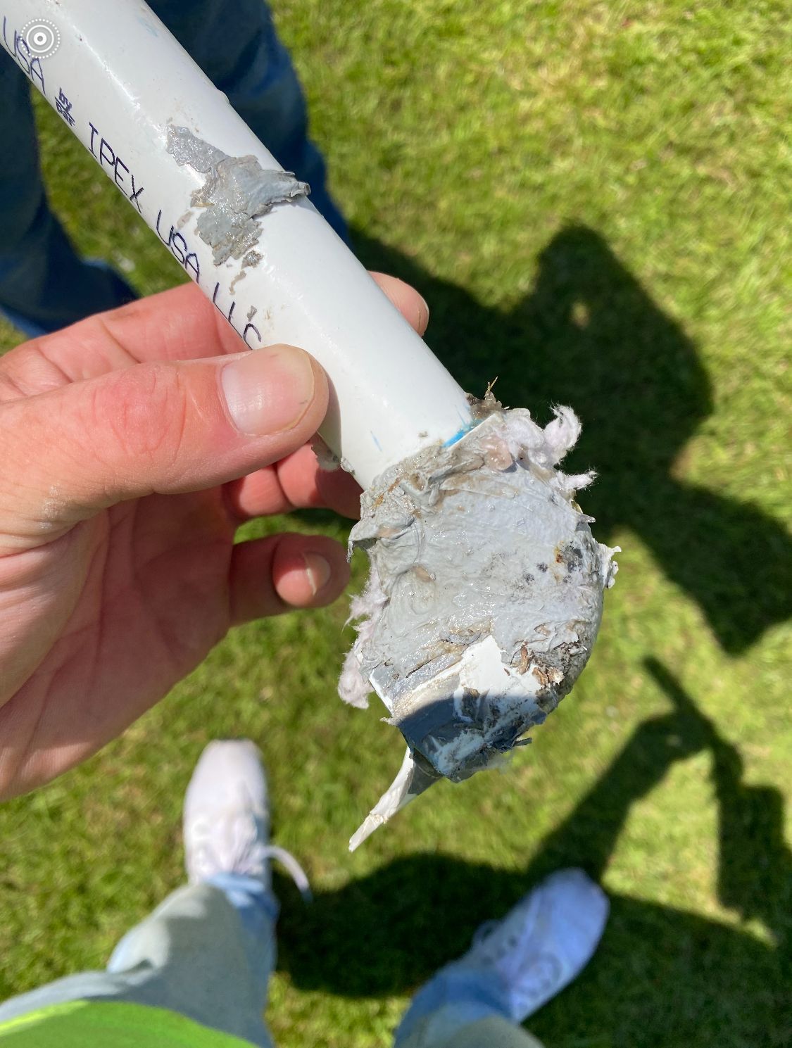 Broken white pole with a jagged end held over grass, with white sneakers visible below.