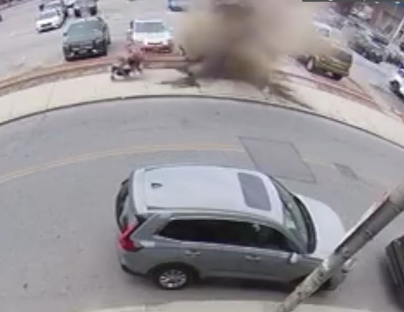 Silver SUV on a street near parked cars, with a large blurred dust or smoke cloud ahead.