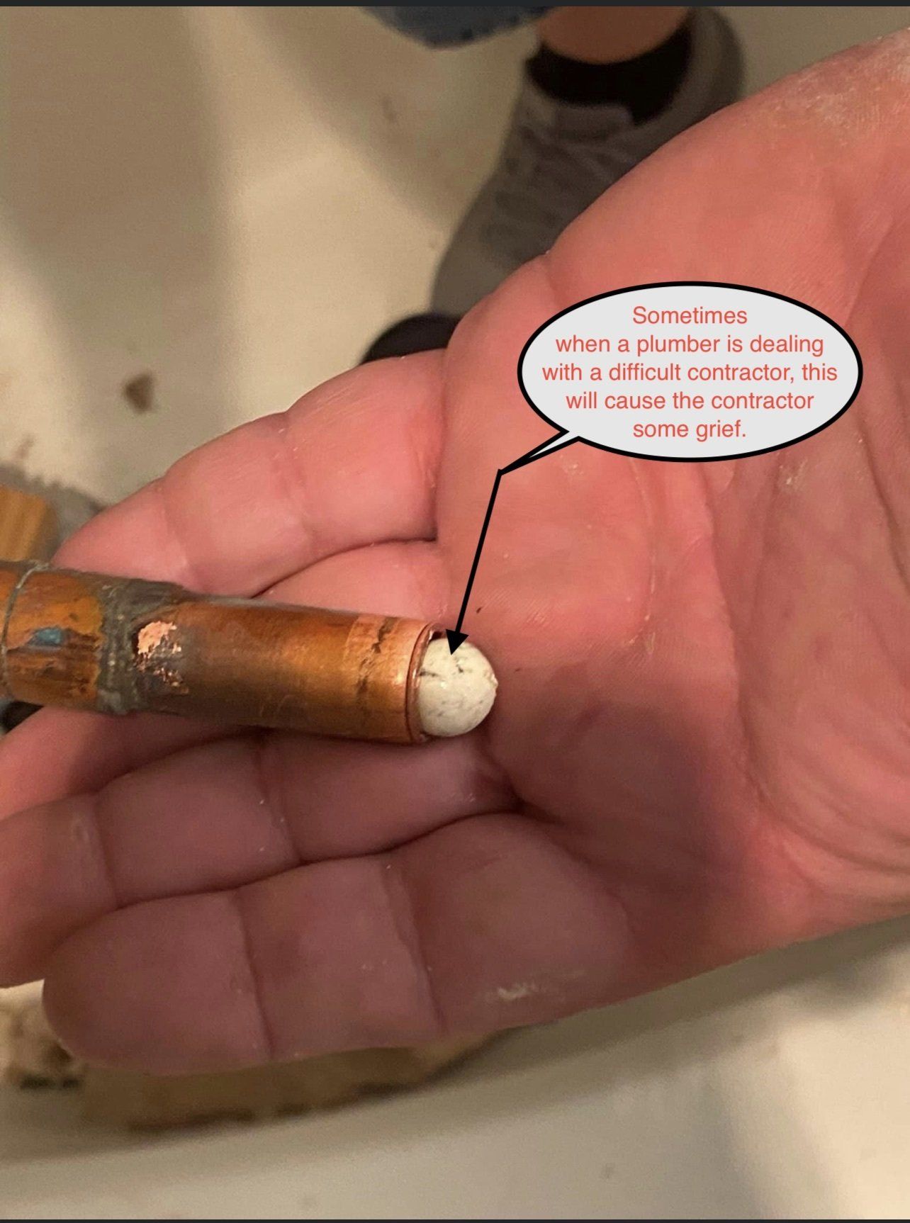 Hand holding a corroded copper pipe with a white cap, shown close up with a speech bubble annotation.