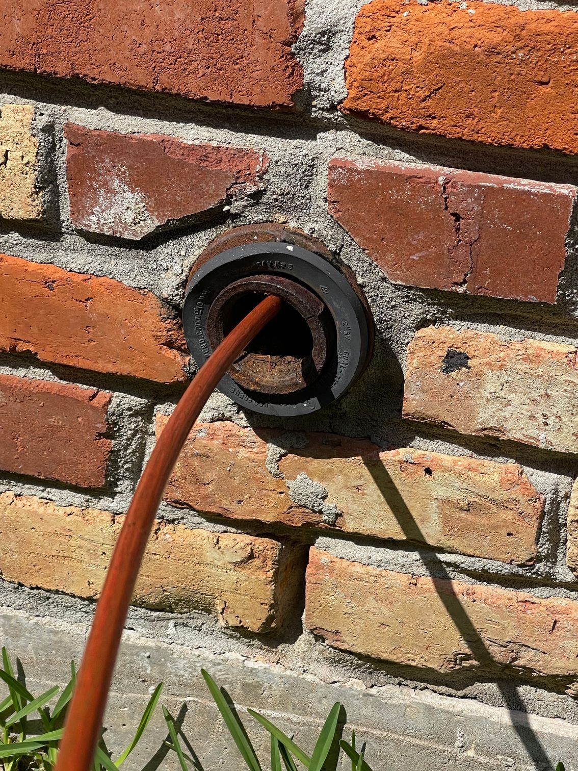 Orange cable entering a black wall vent in a brick exterior wall