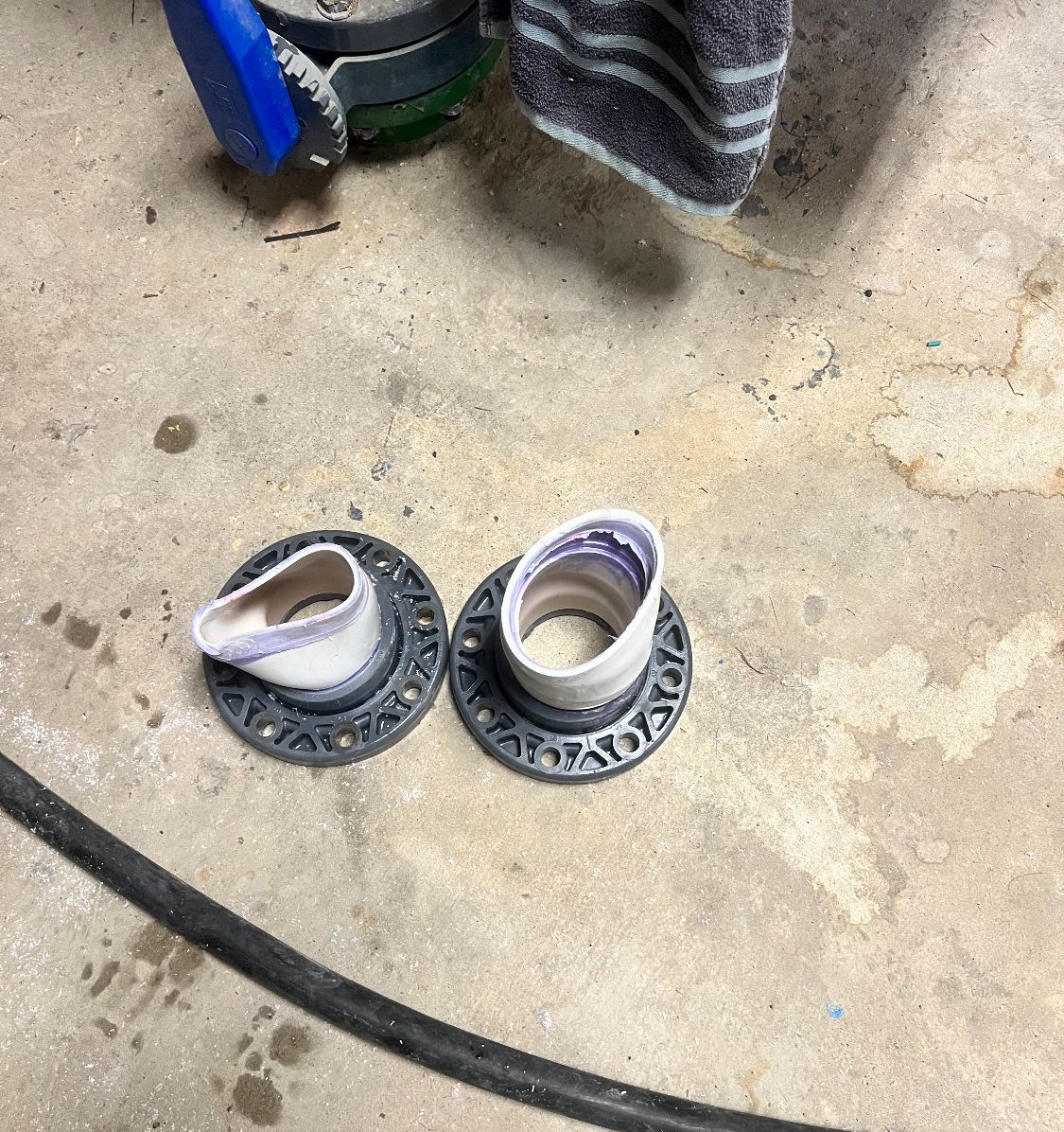 Two gray circular drain flanges on a concrete floor, with white and purple pipe extending from them.