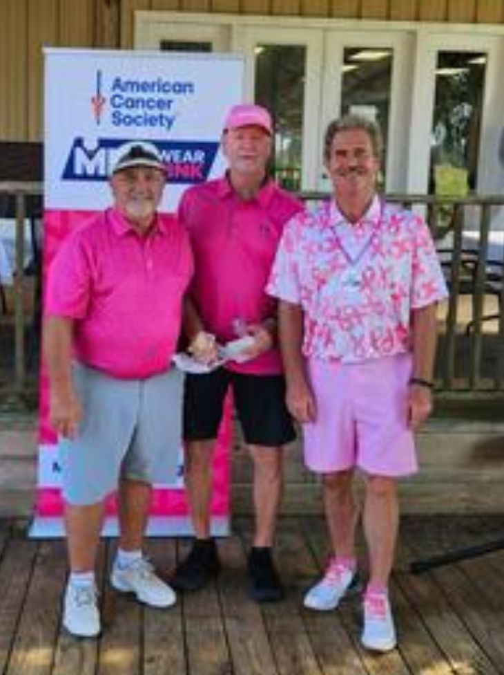Three people in pink outfits posing in front of an American Cancer Society volunteer sign