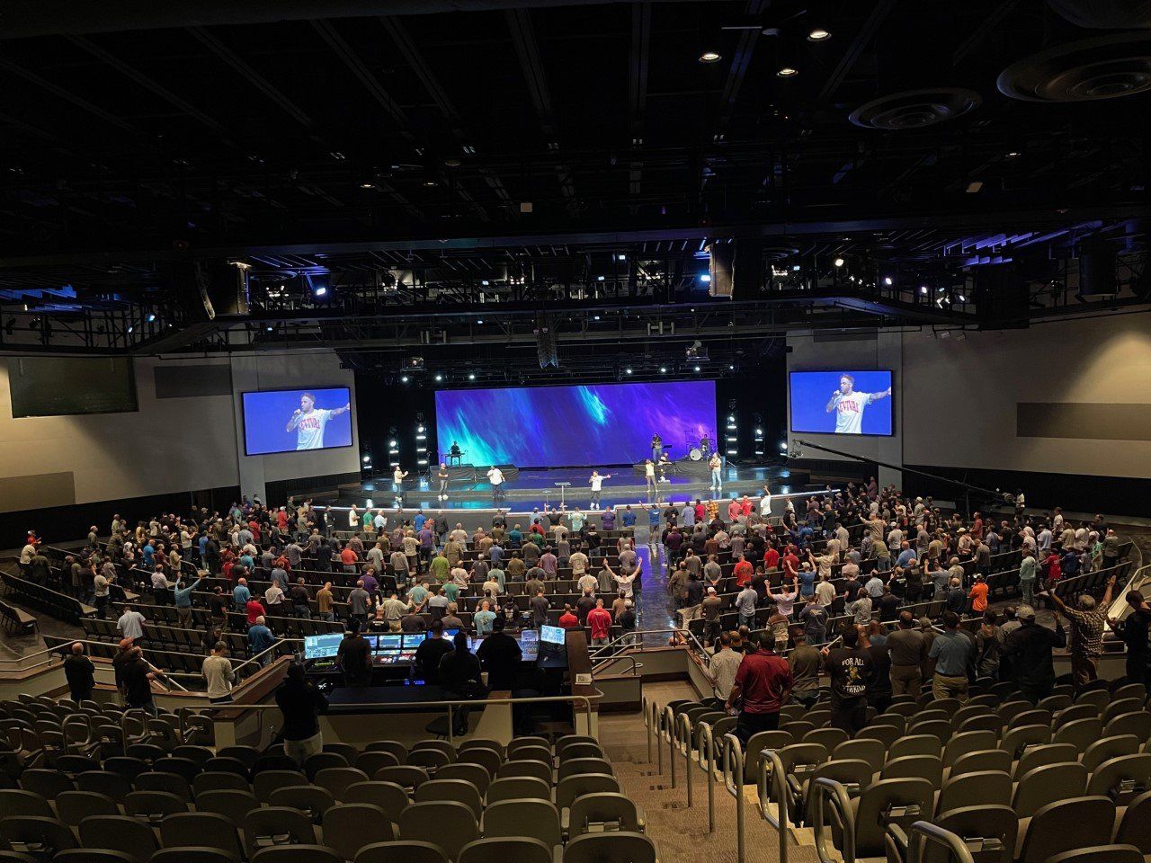 Audience in large hall watching performers on stage with screens.