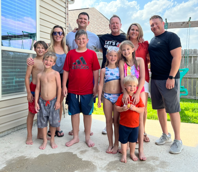 Large group standing together outdoors on a patio, smiling at the camera.